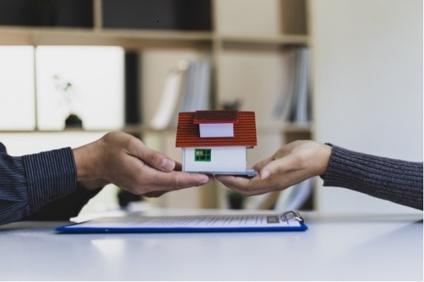 a photo of two people passing a miniature home to each other